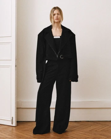 Model standing in a black blazer and matching trousers in a light interior with herringbone parquet flooring.