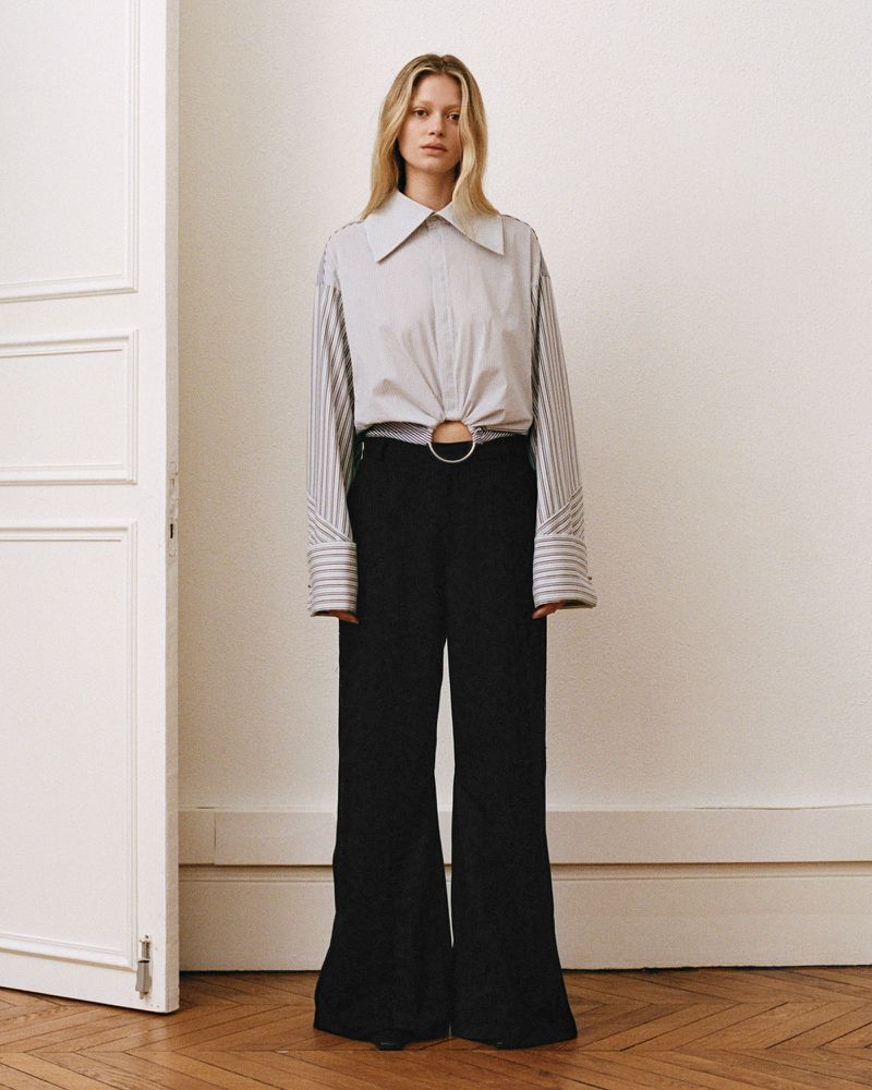 Model standing in a white room wearing a light button-down shirt and black trousers, shot by Royal Gilbert.