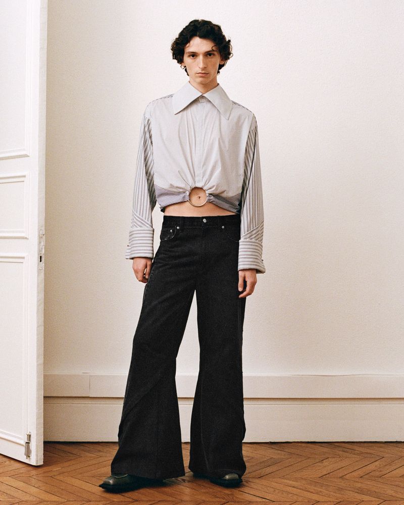 Adult male posing in a photo studio wearing a striped shirt and wide leg pants; fashion editorial photography.