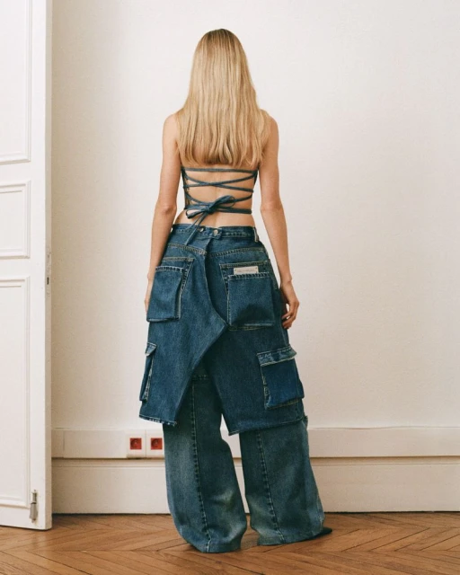 A woman with long blond hair is seen from the back, wearing a denim top and pants with layers of denim pockets. Modern fashion.