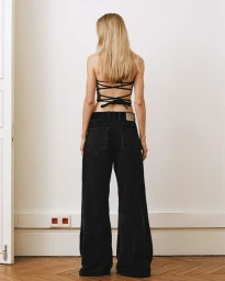 Model seen from behind wearing a black strappy backless top and loose black denim jeans against a white wall.