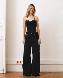 Full-length portrait of a female model wearing a black denim halter top and matching wide-leg trousers against a neutral wall.