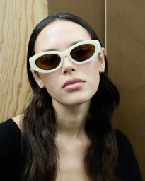 Model wearing white sunglasses and a black top against a wooden wall