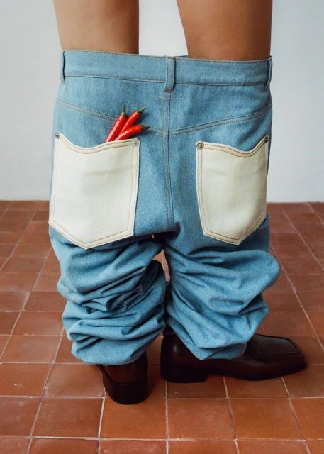 Loose denim jeans worn with brown leather dress shoes, standing on terracotta tile. The jeans have large pockets with red chili peppers.