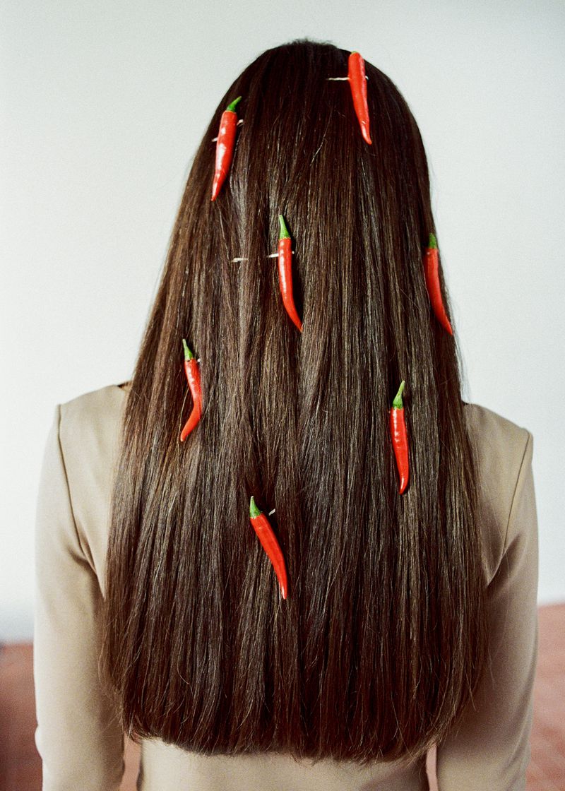 Back view of a woman with long brunette hair styled with red chili peppers. The background is a light beige colour.