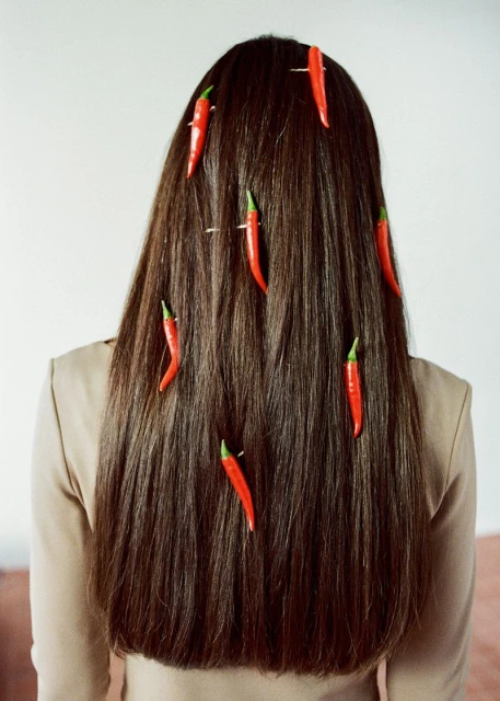 Back view of a woman with long brunette hair styled with red chili peppers. The background is a light beige colour.