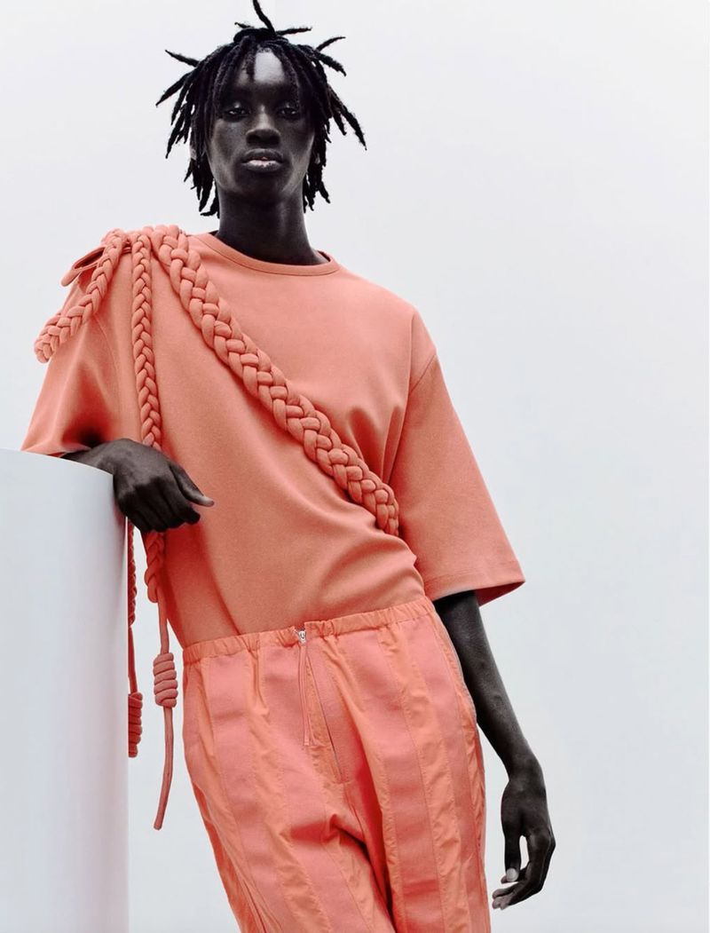 Editorial fashion shot of a male model with dreadlocks wearing a peach-colored casual outfit and standing next to a white column.
