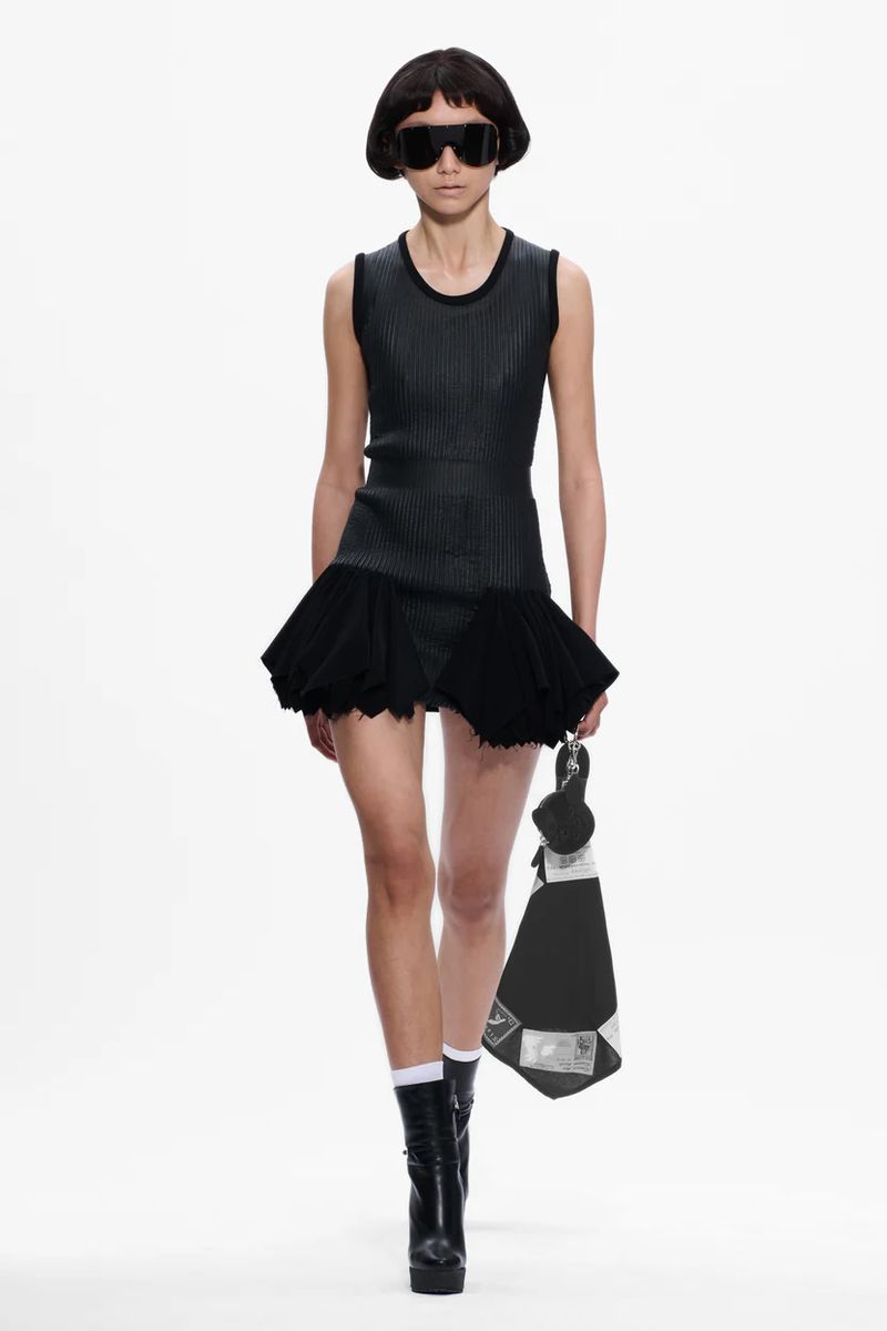 Model in dark sunglasses and black minidress holding a bag against a white background for Stefan Cooke F/W 25