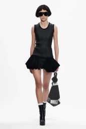 Model in dark sunglasses and black minidress holding a bag against a white background for Stefan Cooke F/W 25