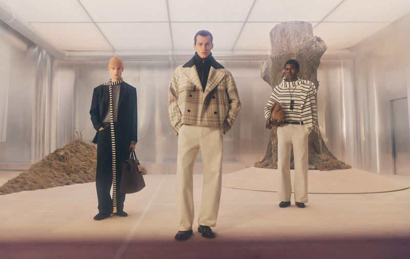 Three male models in contemporary menswear posing inside an industrial metallic set with an abstract artificial tree structure