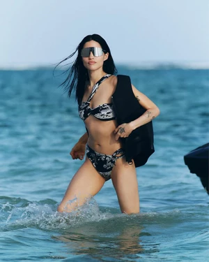 Model Gabbriette wearing a patterned bikini and sunglasses walking through ocean water for H&M