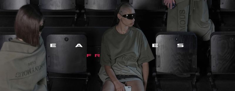 People in olive-green clothing seated in an auditorium, with text overlay and wearing sunglasses, looking stylish and modern.