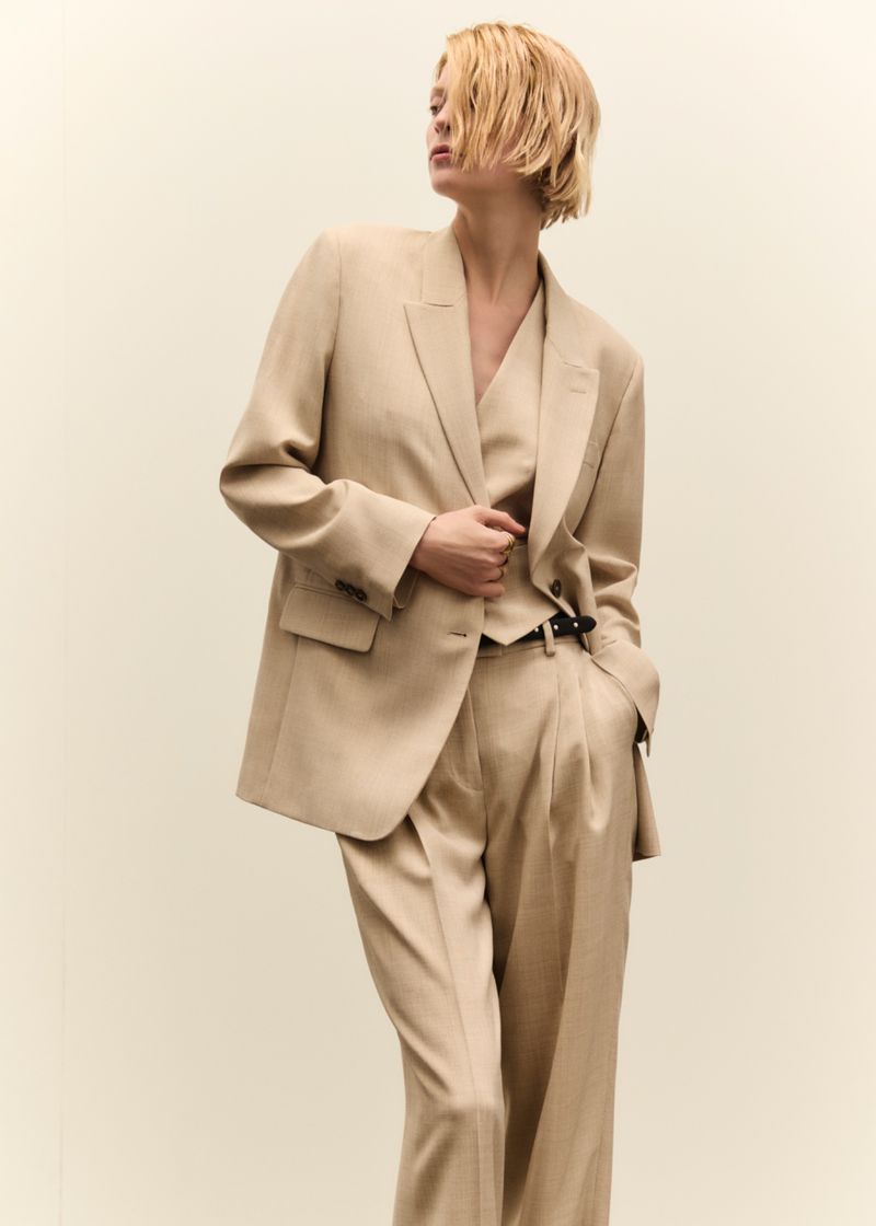 Model wearing a beige tailored suit jacket and matching trousers against a neutral background