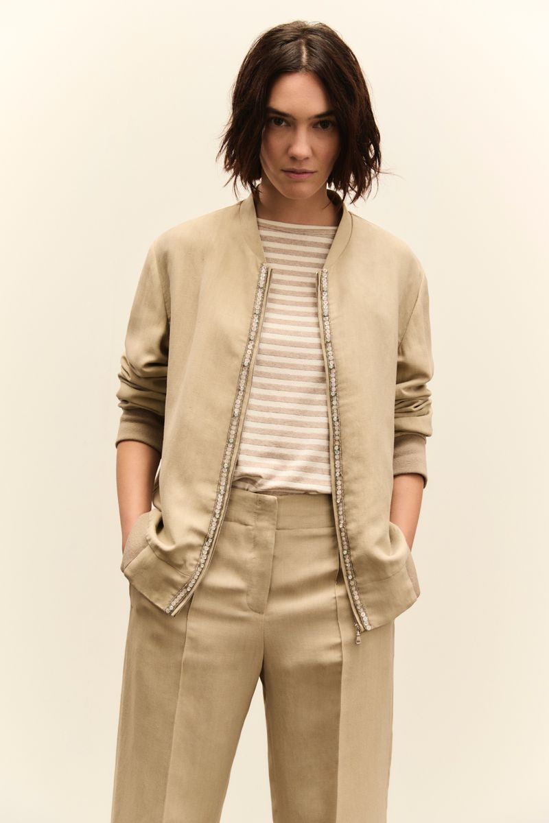 Model wearing a beige jacket and trousers with a striped top against a plain studio background.