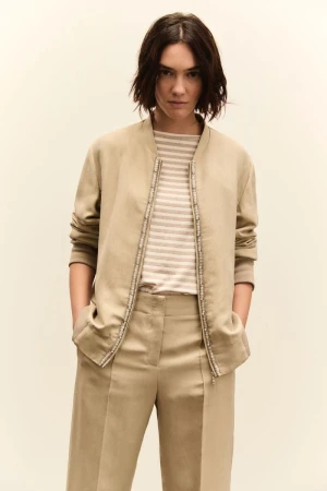 Model wearing a beige jacket and trousers with a striped top against a plain studio background.
