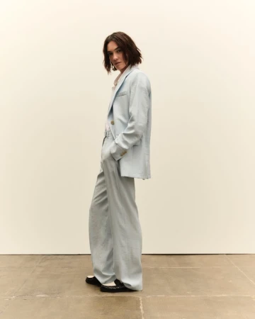 Model wearing a light blue suit jacket and matching trousers standing against a plain backdrop.