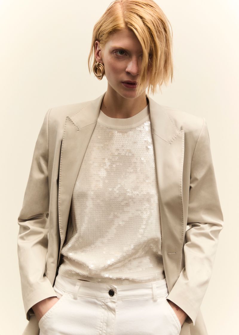 Model in cream blazer and sequin top against plain background