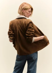 Model with blonde hair wearing a brown suede jacket and blue jeans against a neutral background