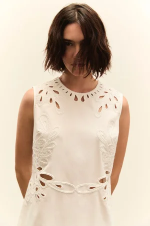 Model in white cut-out dress with dark shoulder-length hair against a plain light background for Seventy Venezia SS25