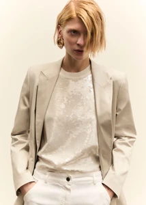 Model in cream blazer and sequin top against plain background