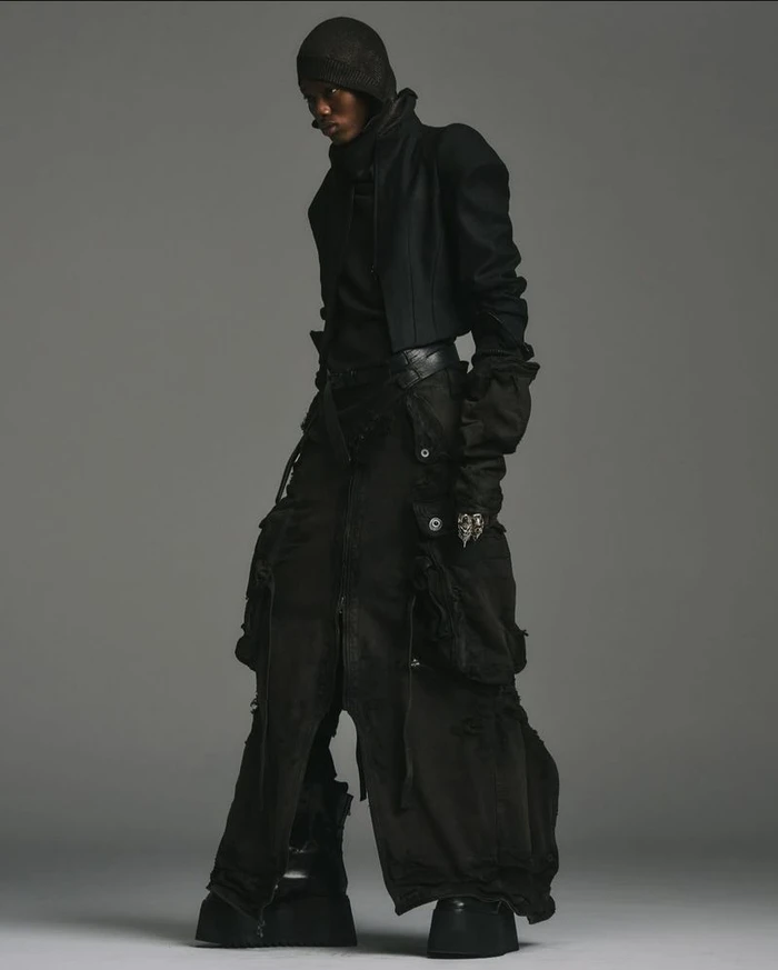 Model in black layered outerwear with a fitted beanie and chunky platform boots against a plain grey background