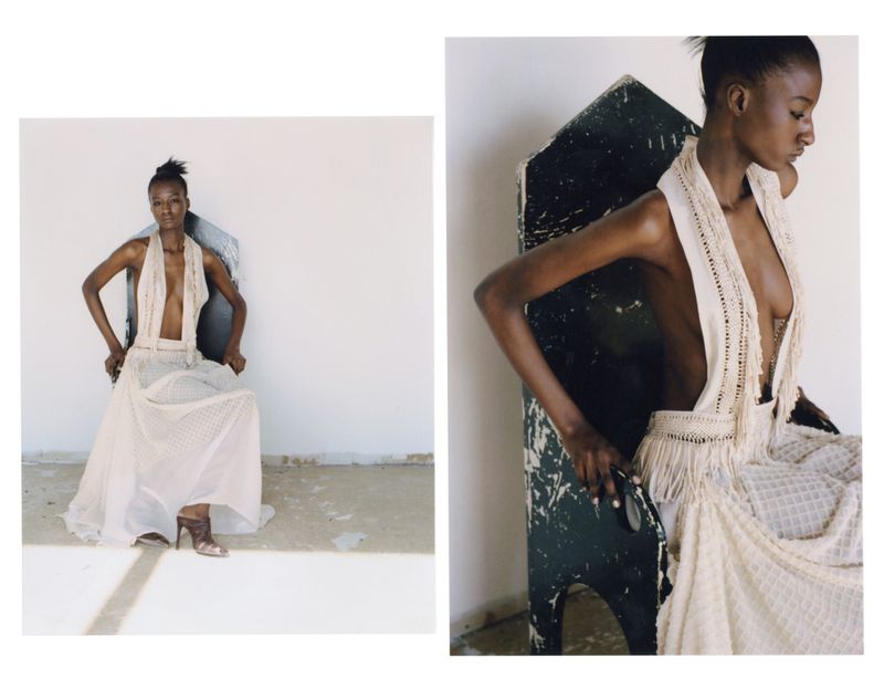A Black female model sits on a chair in a photo studio, wearing a white gown with fringe detail, showcasing a fashion editorial style.