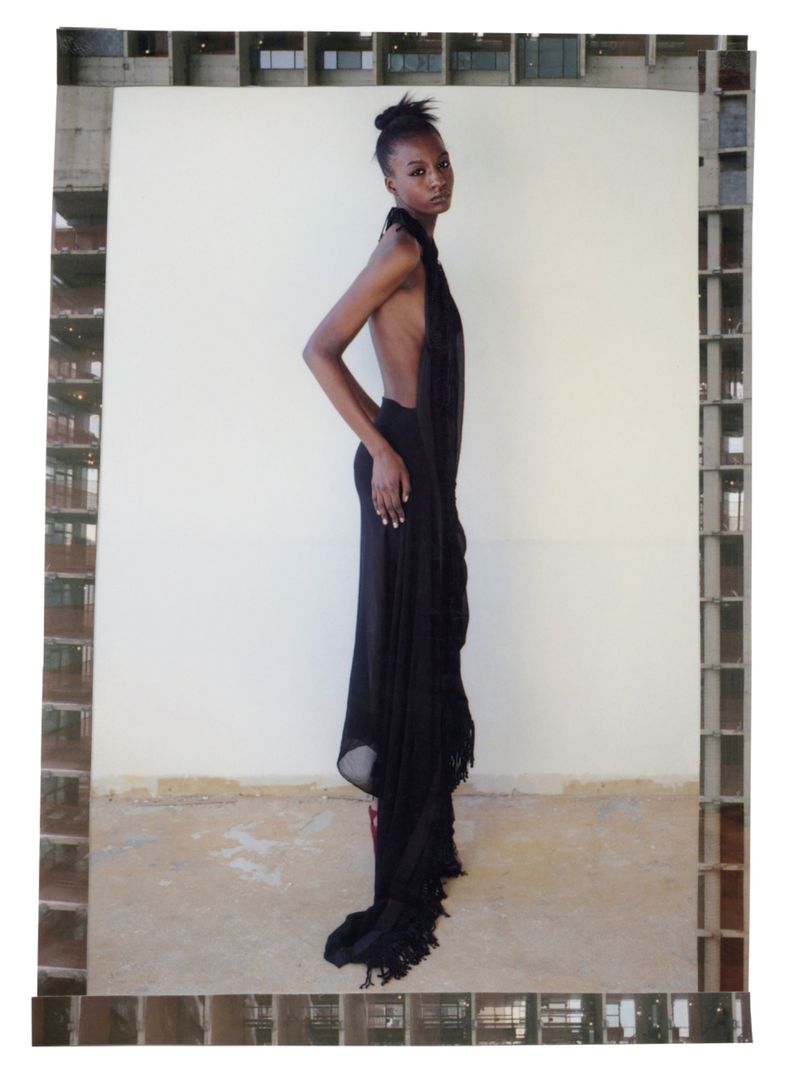 An African American woman poses in a black halter dress, captured in a full shot against a cream backdrop, framed by an architectural border.