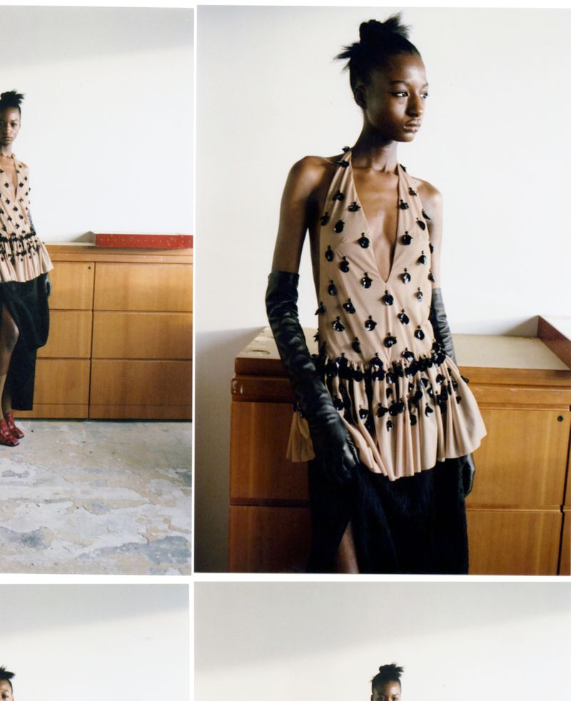 Fashion shot of a black female adult wearing a tan halter top and black skirt, posing in an indoor environment near wood cabinets.