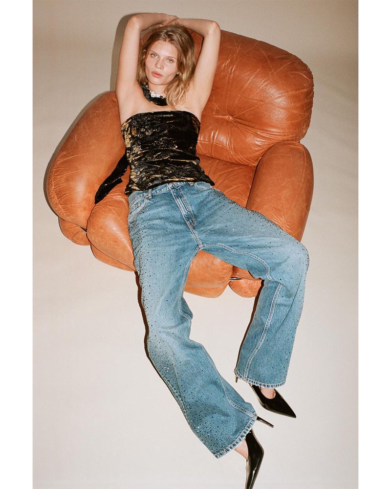 Model Ida Heiner leaning back in a large brown leather armchair wearing a black patterned top and blue jeans
