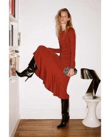 Fashion shot of an adult woman in a red dress and black boots holding a zebra print purse posing next to a bookshelf indoors.
