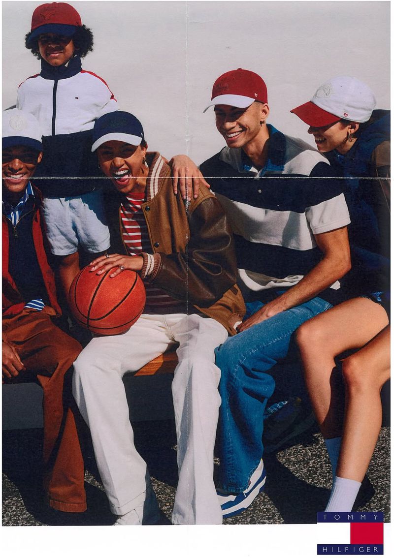 Group of diverse young adults in casual clothing, some with baseball caps, sitting and holding a basketball in an outdoor setting.