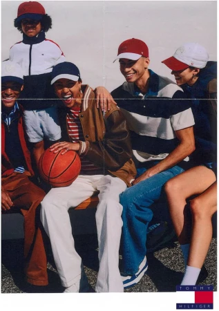 Group of diverse young adults in casual clothing, some with baseball caps, sitting and holding a basketball in an outdoor setting.