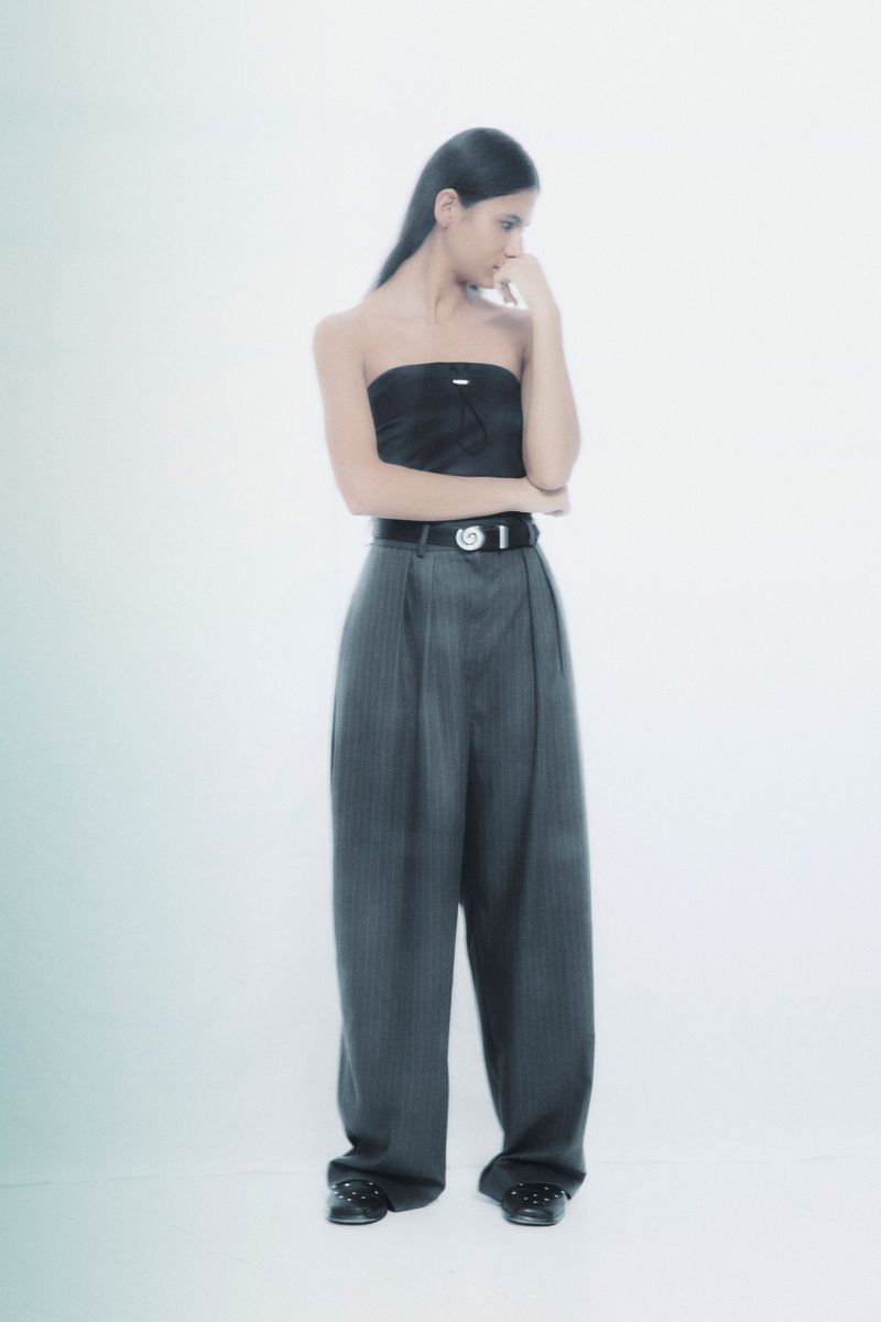 Young woman in pinstripe pants and tube top poses pensively in a bright studio environment. Fashion-forward, confident, and stylish.