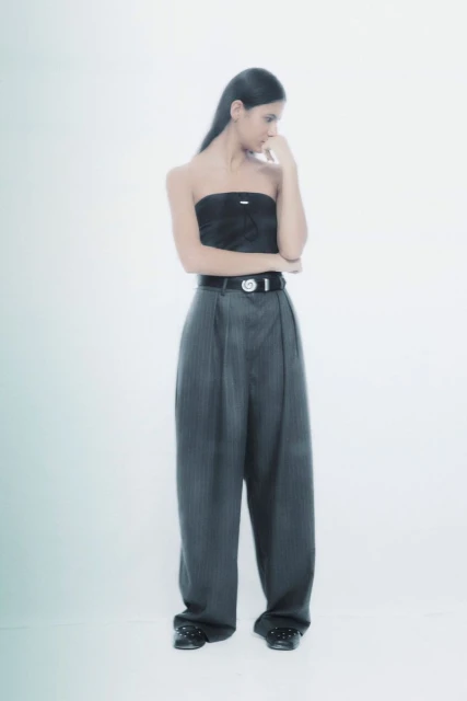 Young woman in pinstripe pants and tube top poses pensively in a bright studio environment. Fashion-forward, confident, and stylish.