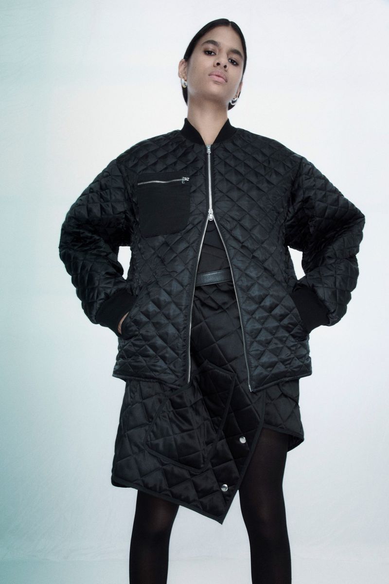 Fashionable adult female poses in black quilted jacket and skirt in a studio against a gradient background. Minimalist studio fashion shot.