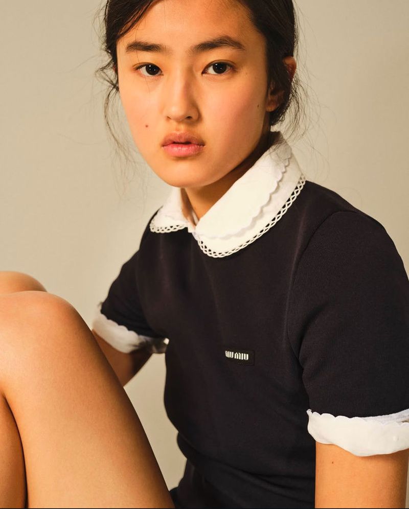 Portrait of an Asian female model wearing a navy dress with a white lace collar. The image is shot in a photo studio with a neutral background.