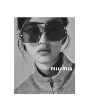Close-up portrait of a model wearing oversized sunglasses and a grey zip-up jacket against a plain background.