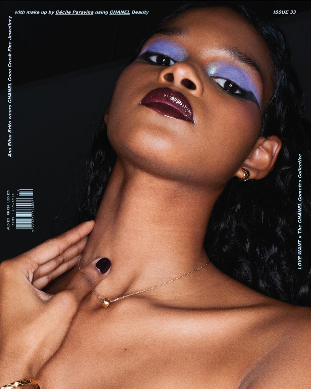 Close-up beauty portrait of a woman with dark skin and bold purple eyeshadow and dark glossy lips, wearing jewelry, against a black backdrop.