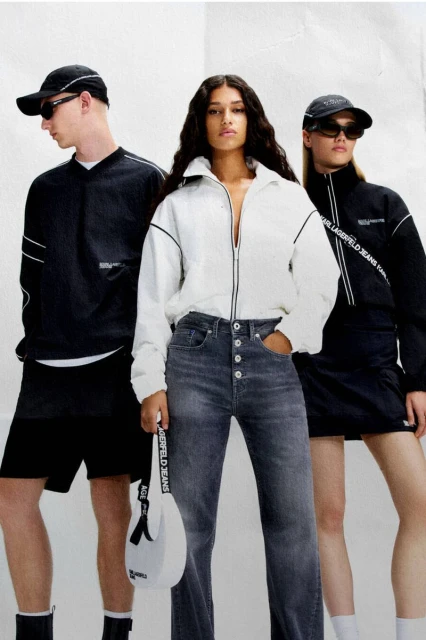 Three fashion models showcase Karl Lagerfeld Jeans apparel; woman in the middle wearing white jacket and grey jeans; the other two are wearing black.