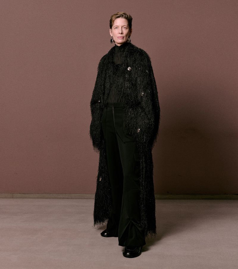 Model standing against a plain brown background wearing a textured black long coat and dark trousers for William Fan AW25 lookbook.