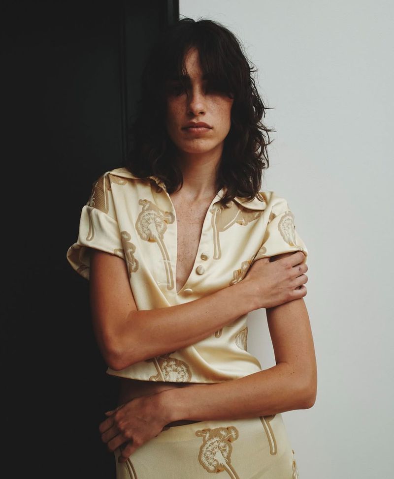 Brunette woman in patterned cropped shirt with crossed arms posing against a black and white wall in a fashion shot.