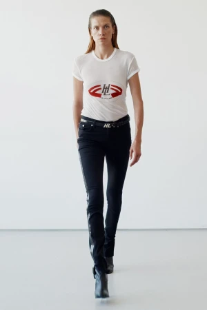 A woman in a white tee and black pants walks towards the camera in a stark white setting. Modern fashion, studio lighting, minimalist design.