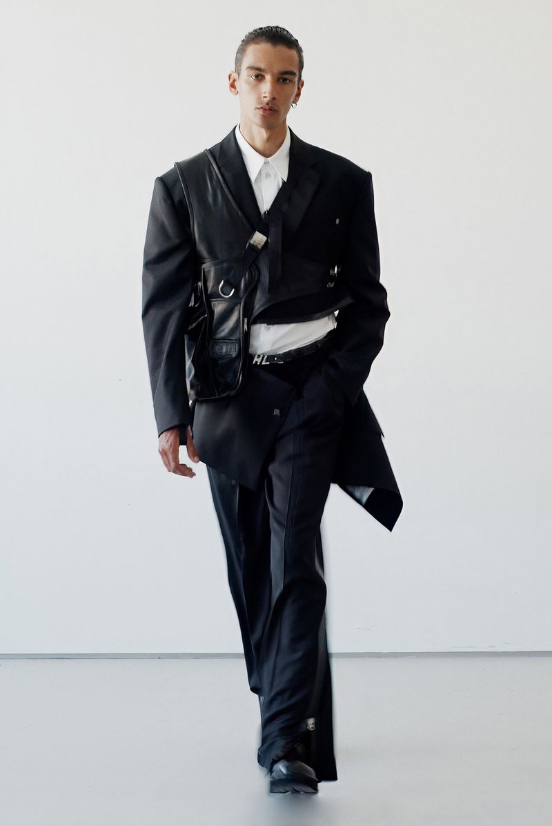 Model in black suit with harness and white shirt against a white seamless background for Helmut Lang