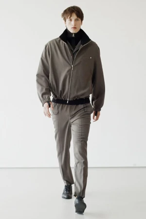 Model wearing a taupe zip jacket and matching trousers against a plain white studio wall