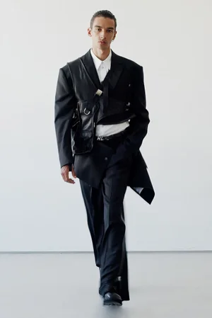 Model in black suit with harness and white shirt against a white seamless background for Helmut Lang