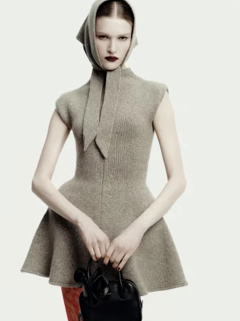 Model wearing a grey knitted peplum dress with a matching headscarf and holding a black handbag against a plain background