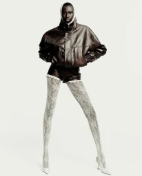 Model wearing a dark brown leather jacket and shorts with white lace tights against a plain white background.