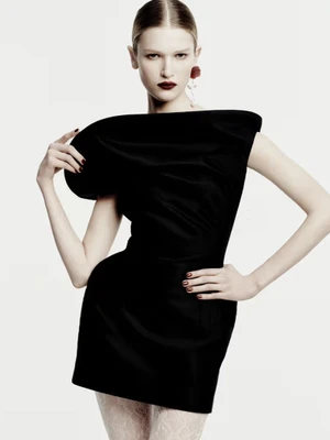 Model wearing a structured black dress and red earrings against a white background for Magda Butrym