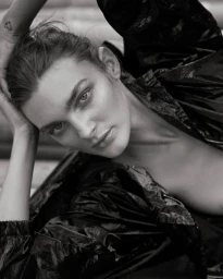 Close-up monochrome portrait of a woman with her hands behind her head wearing a glossy black jacket for Relik Editions