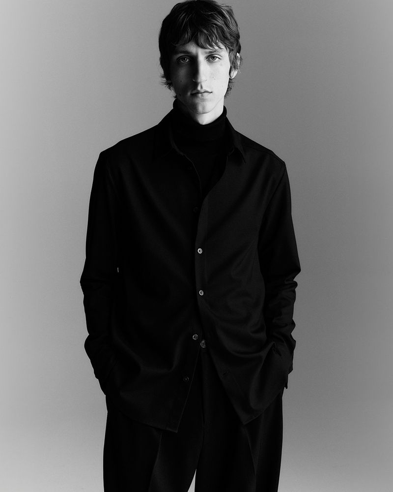 Monochrome portrait of a young male model wearing a dark button-down shirt and turtleneck against a grey gradient background
